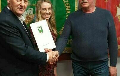 trzy osoby podajace sobie rękę i przekazujące teczkę z umową 